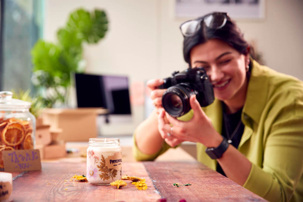 Smiling woman photographing a candle on wooden table.
